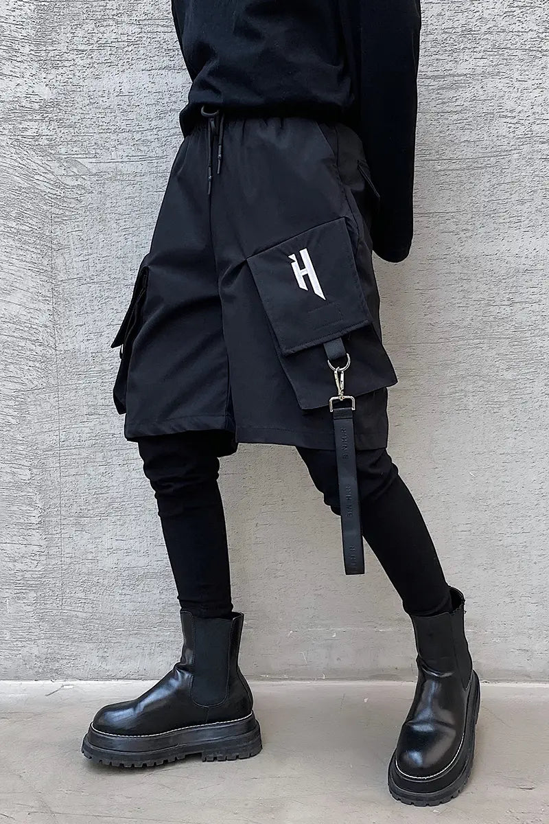 Black cargo shorts featuring multiple pockets, a prominent white h logo on the thigh pocket, and a detachable strap designed for hip hop style pants.