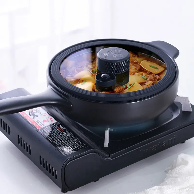 Black ceramic micro pressure anti overflow casserole pot with glass lid and textured knob resting on a matching black electric stove.