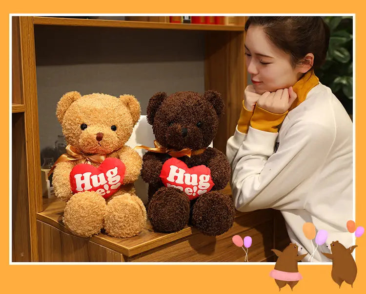 Zwei plüschige Teddybär-Plüschtiere, weiche Stofftierpuppen, in hellbraun und dunkelbraun, die rote herzförmige Kissen halten, mit der Aufschrift „Hug me“ in Weiß.