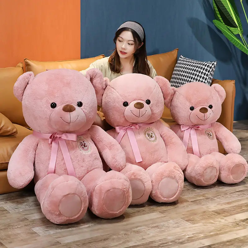 Drei kuschelige rosafarbene Teddybären mit weichem Fell, bestickten schwarzen Knopfaugen, angenähten Lächeln und passenden rosafarbenen Schleifenborten um den Hals, ideal als Teddybären mit Liebesbändern für Kinder und Mädchen.
