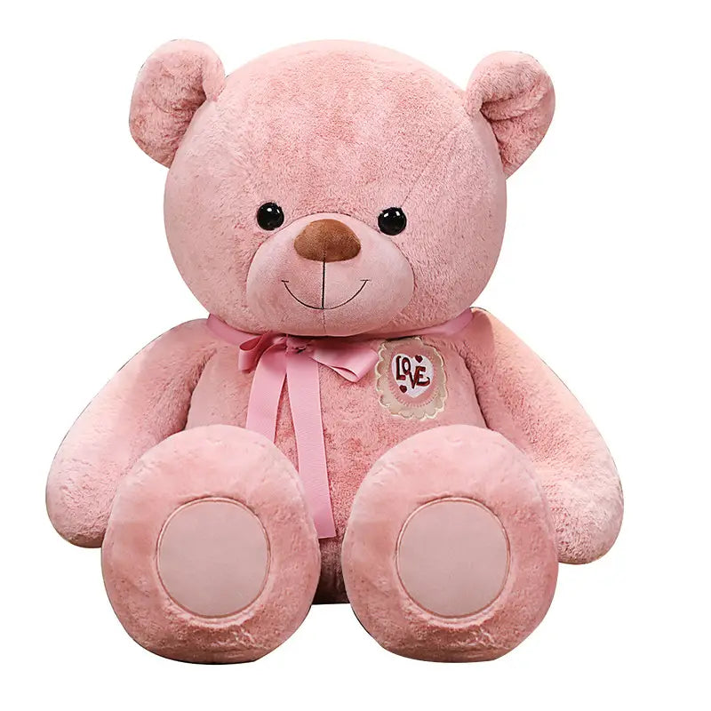 Ein kuscheliger rosafarbener Teddybär mit schwarzen Knopfaugen, einer braunen Nase, einem angenähten Lächeln, einem bestickten Liebes-Patch auf der Brust und einer passenden Schleifenborte um den Hals, entworfen für Kinder und Mädchen.