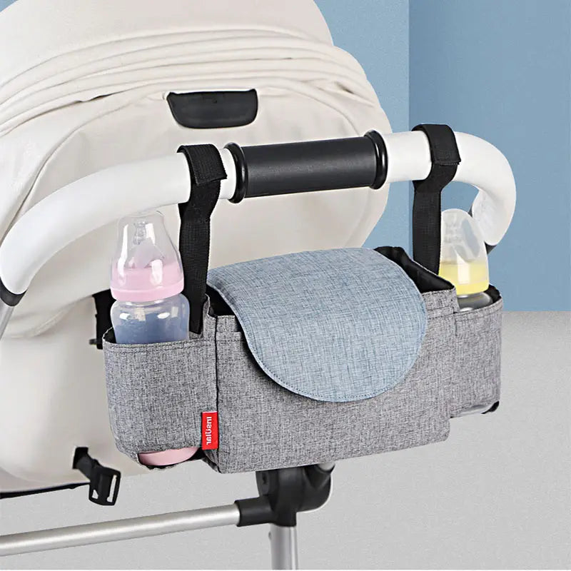 Gray textured fabric stroller organizer bag with multi storage pockets featuring black straps and a light blue flap for convenient stroller attachment.