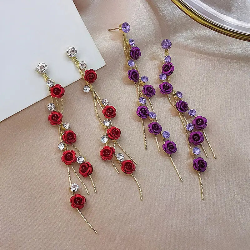 Elegant rose tassel drop earrings featuring cascading red and purple rose charms accented with clear rhinestones and pearls on gold-toned metal wires.