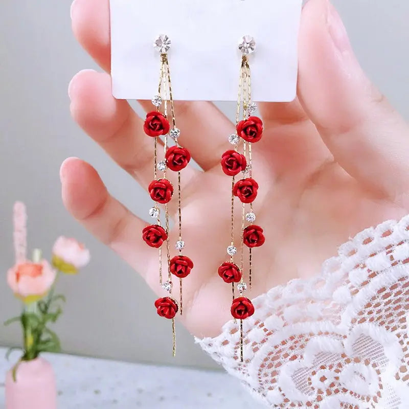 Elegant rose tassel drop earrings featuring red rose-shaped designs with gold-toned chains and clear crystal accents.