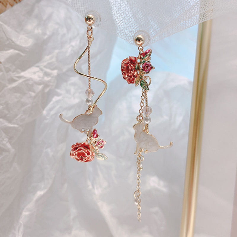 Elegant rose tassel drop earrings with rhinestones and pearls featuring delicate gold-toned dangling translucent white cat charms and vibrant red enamel roses with green leaves accented by clear crystal beads.