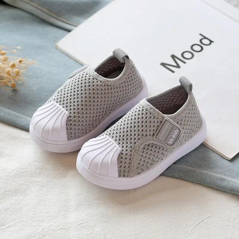 Breathable gray mesh slip-on sneakers for toddlers and kids with white rubber toe caps and soles featuring a velcro strap for easy wear.
