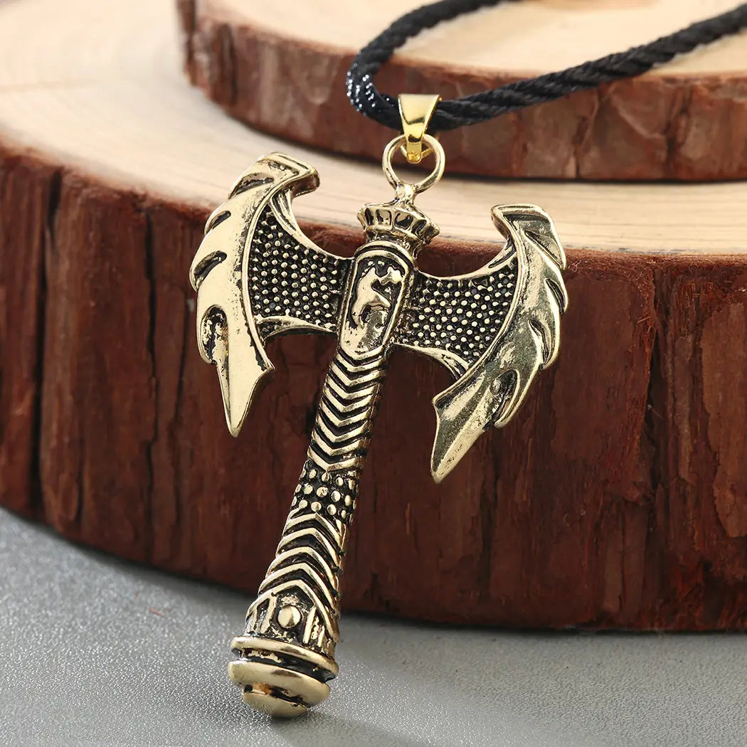 Gold-colored intricately detailed viking axe pendant with textured blade and patterned handle on a braided cord necklace.