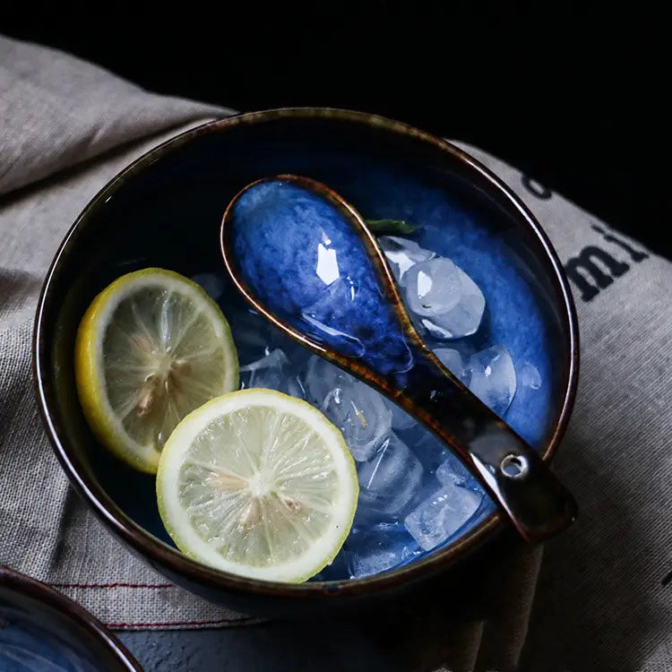 Deep blue ceramic spoon kiln glaze porcelain tableware bowl with a rustic brown rim holding ice cubes and sliced lemons alongside a matching spoon.