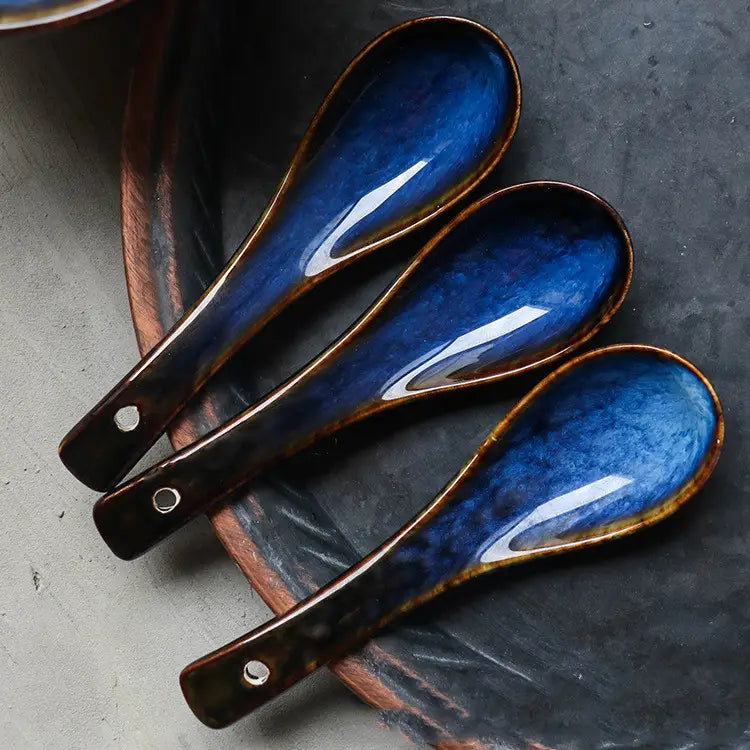 Set of three blue ceramic soup spoons with glossy kiln glaze porcelain finish and brown rim featuring a small hole near the handle end for tableware use.