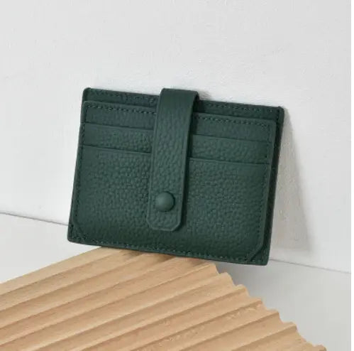 Dark green textured leather ultra thin minimalist card holder with matching flap and button closure and attached strap.