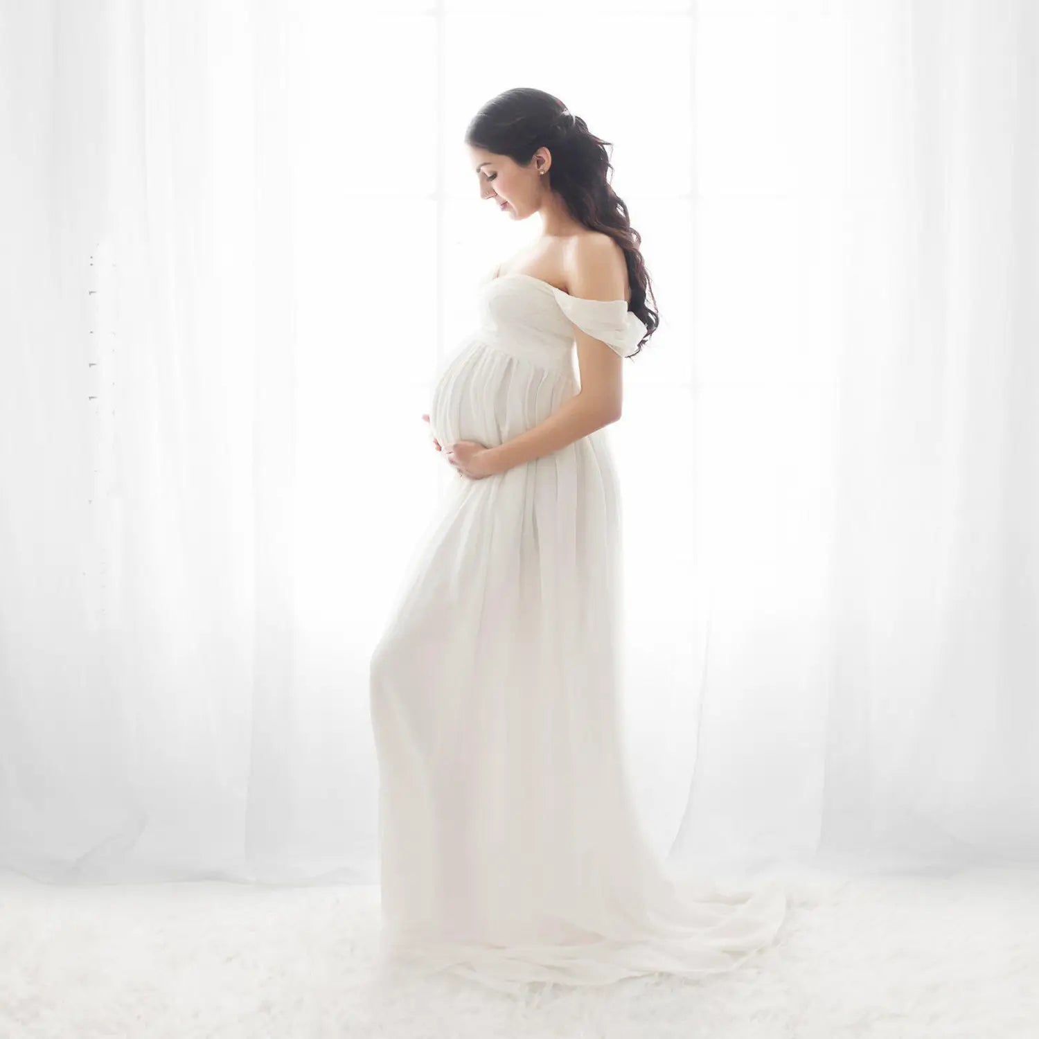 a flowing off the shoulder white chiffon maternity gown with soft airy fabric and delicate detailing at the neckline designed for photoshoots