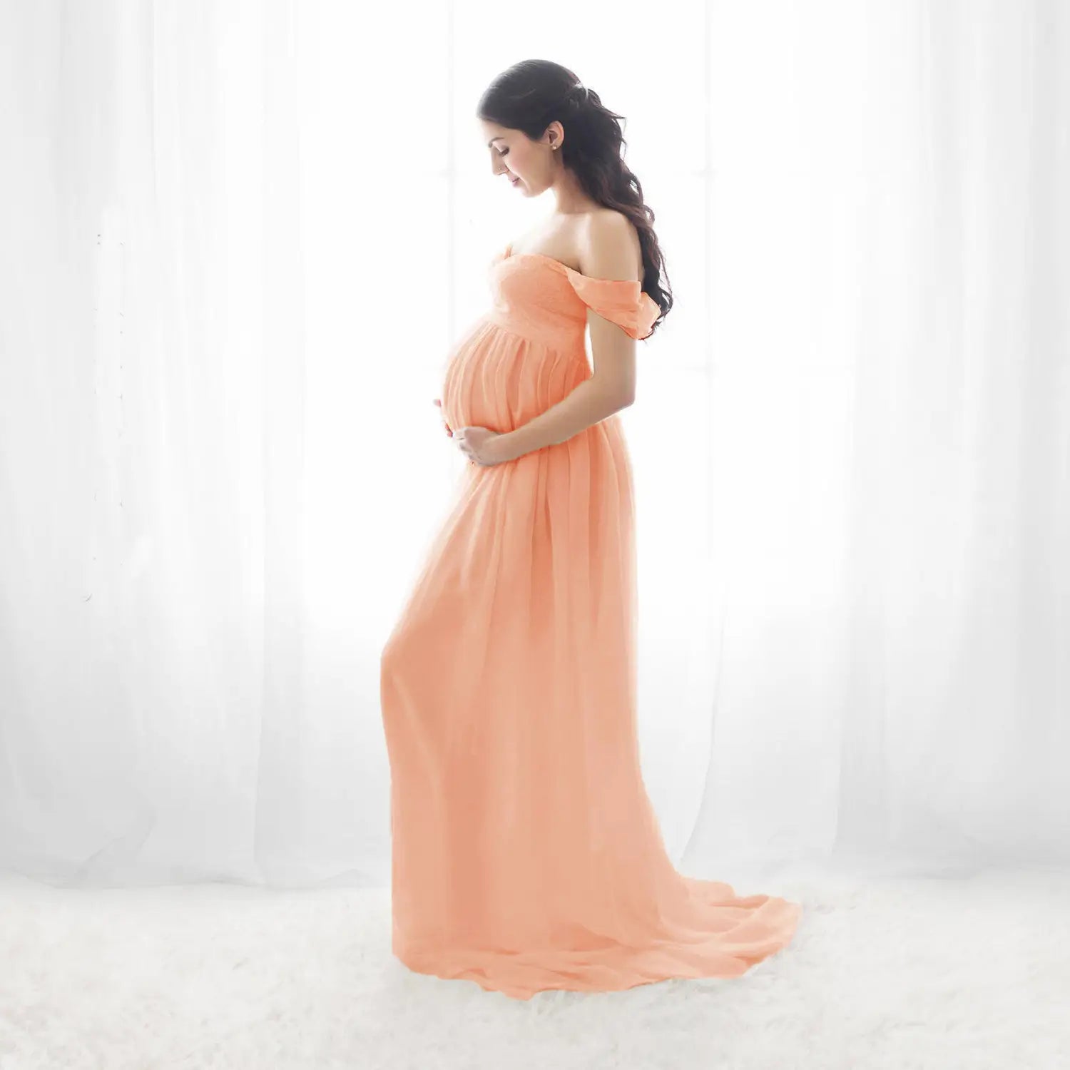 a flowing peach-colored chiffon maternity gown with off the shoulder sleeves and a soft draped silhouette designed for photoshoots