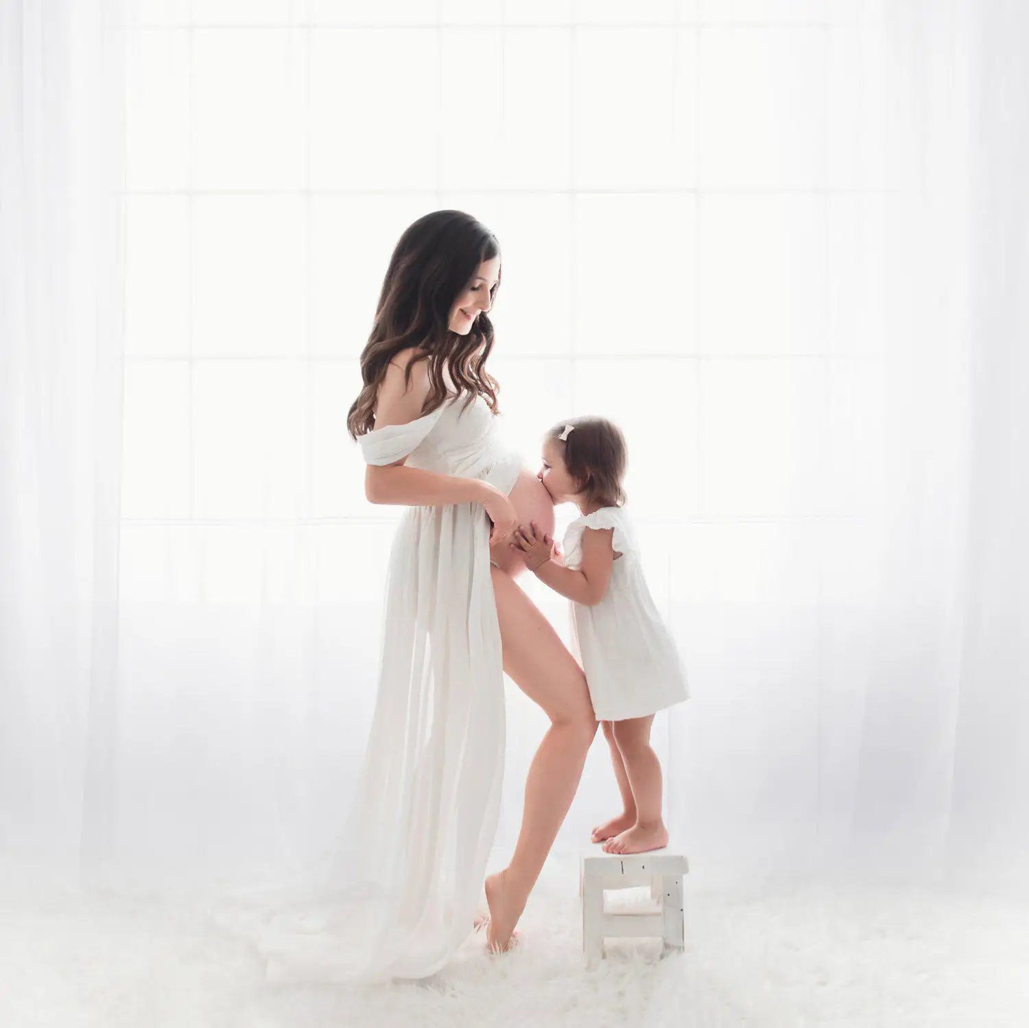 a flowing white off the shoulder chiffon maternity gown with a long sheer skirt designed for photoshoots