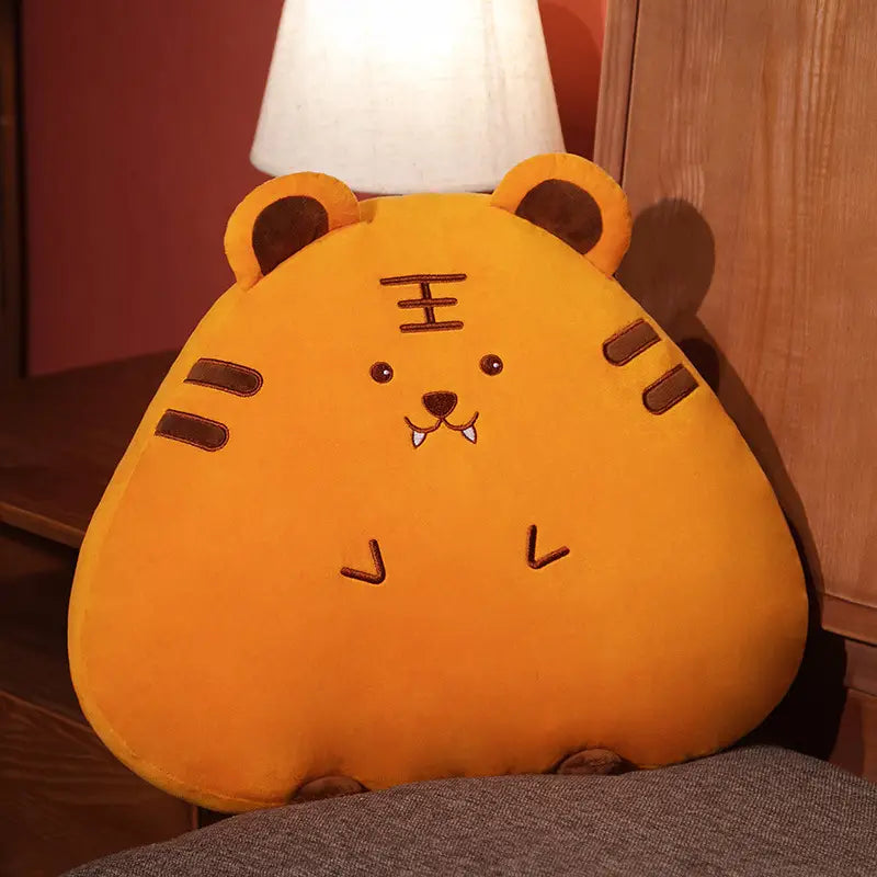 Ein orangefarbenes Kuschel-Tiger-Kissen mit bestickten braunen Gesichtszügen und Ohren aus der Kollektion der Kuscheltiertier-Kissen Kaninchen Schwein Huhn, in 45 cm und 65 cm.