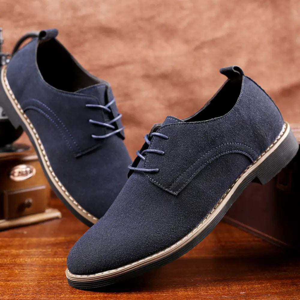 Chaussures habillées en daim oxford à lacets pour hommes bleu marine, avec surpiqûres ton beige contrastées et un talon bas, présentées depuis l’arrière
