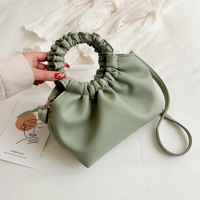 A soft sage green ruched leather bucket bag with a gathered top handle and adjustable shoulder strap.