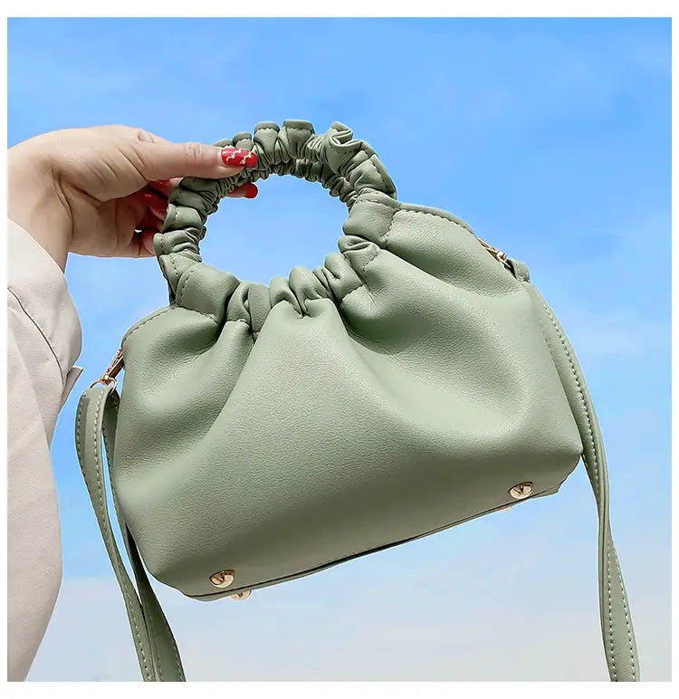 A soft sage green ruched leather bucket bag with a gathered elasticated top handle and matching adjustable strap.
