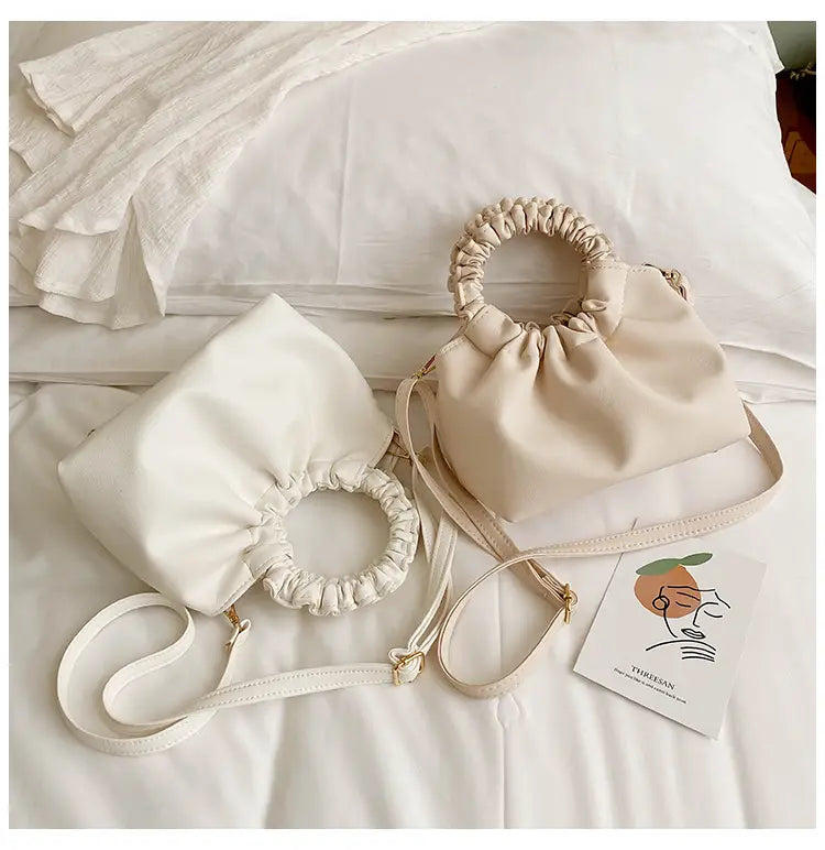 Cream-colored faux leather ruched leather bucket bag with gathered top handle and adjustable shoulder strap.