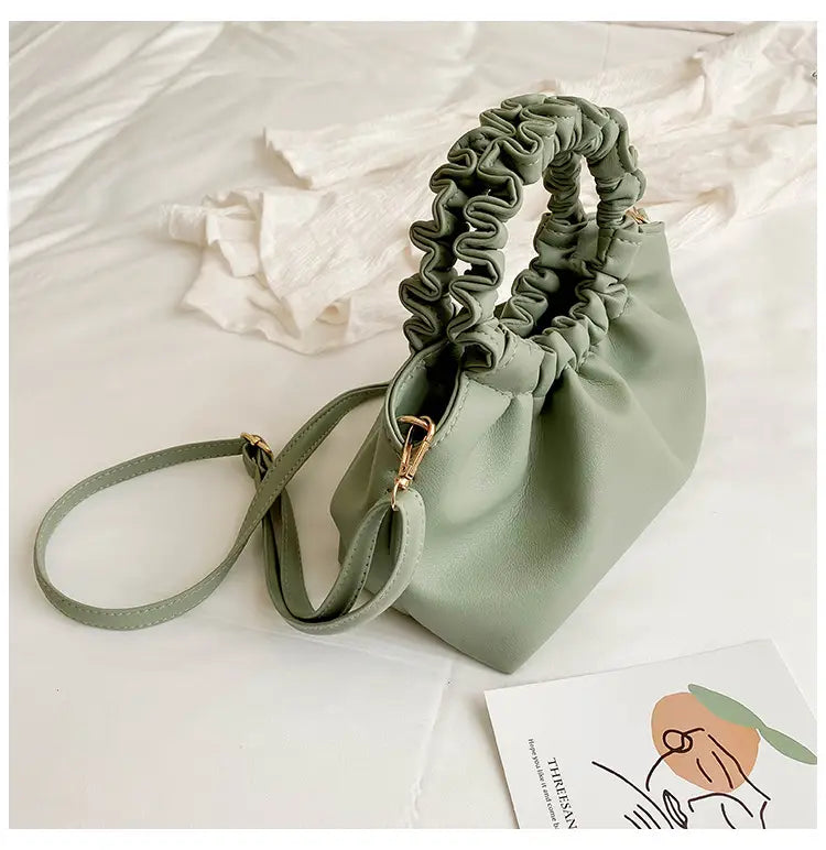 A soft sage green ruched leather bucket bag with an elasticated top handle and adjustable shoulder strap.