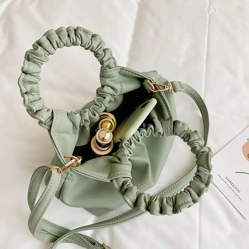 A ruched leather bucket bag in soft sage green featuring gold-tone hardware and a detachable adjustable strap.