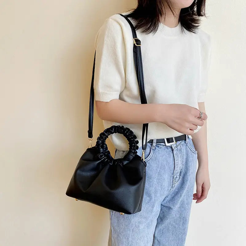 Black leather ruched bucket bag with braided handle gold tone hardware and adjustable strap.