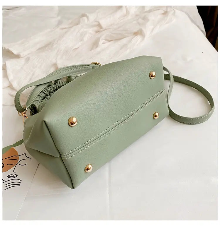 A soft sage green ruched leather bucket bag made of faux leather featuring gold-tone studs and a drawstring top closure with an adjustable strap.