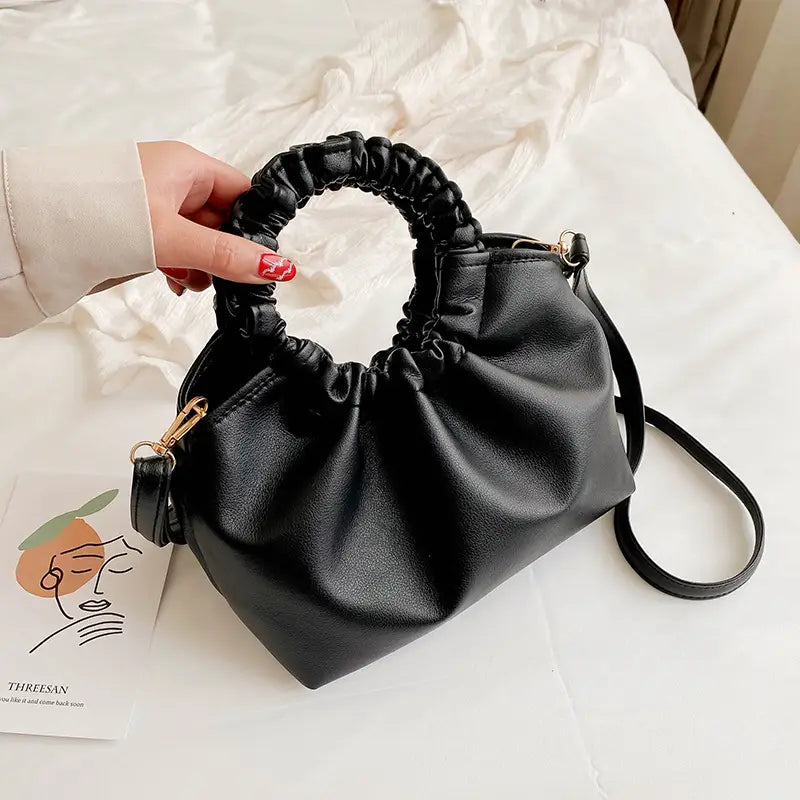 Black ruched leather bucket bag featuring a braided top handle and an adjustable shoulder strap