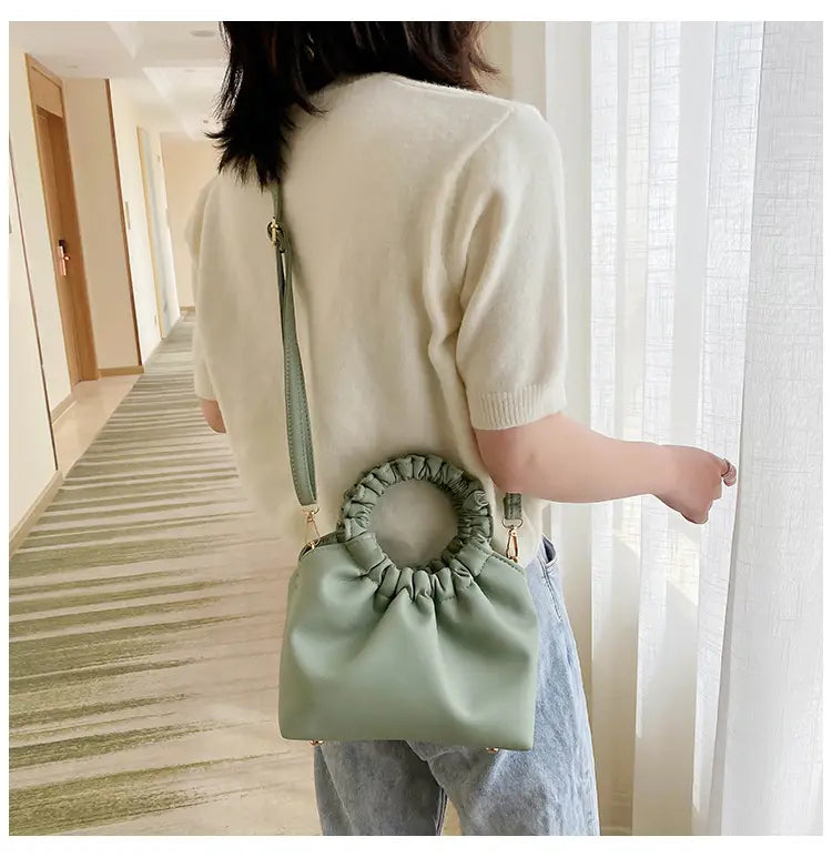 Mint green faux leather ruched leather bucket bag with circular handle and adjustable strap shown from the front.