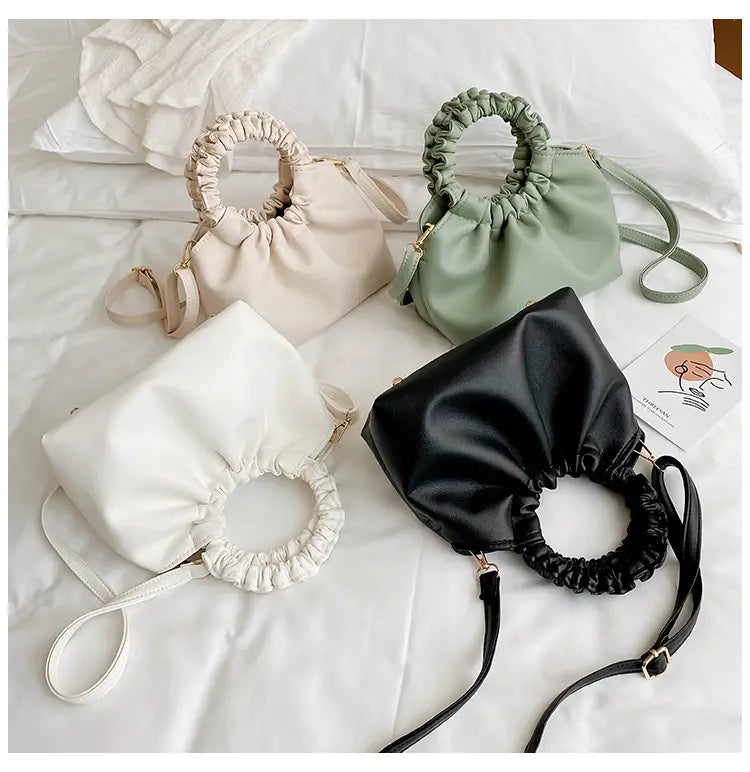 Four stylish ruched leather bucket bags in cream sage green white and black faux leather with adjustable straps and circular ruched handles.