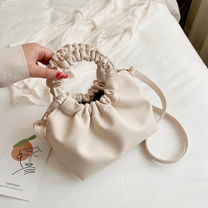 Beige ruched leather bucket bag featuring a drawstring closure with a gathered top handle and a matching adjustable strap.