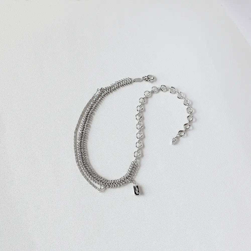Silver-toned layered chain bracelet featuring a small black rectangular charm, complementing the textured heart link silver necklace with black charm.