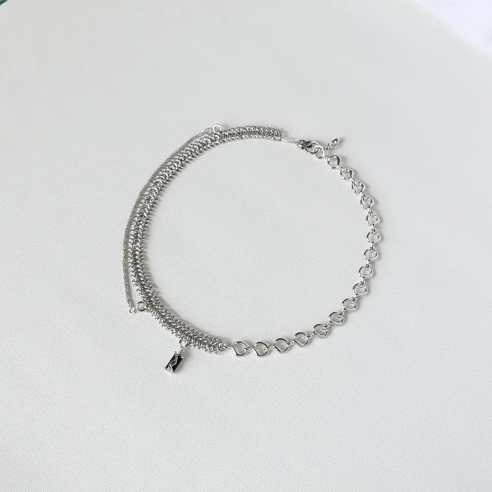 Silver chain necklace featuring a layered design with intricate mesh and heart-shaped links accented by a small black charm in a textured heart link silver necklace with black charm.