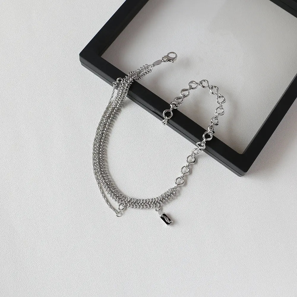 Silver chain bracelet with a layered design featuring intricate mesh and heart-shaped links accented by a small black charm in a textured heart link silver necklace with black charm.