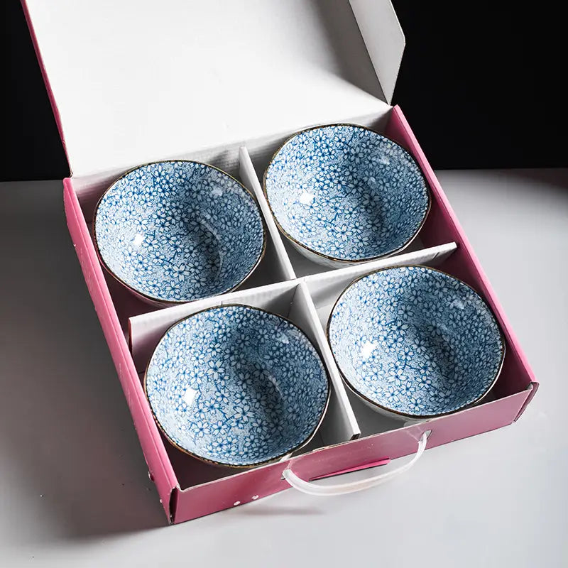 Set of four blue ceramic bowls with delicate white floral patterns and gold-rimmed edges nestled in a pink gift box featuring floral gold rim porcelain design five inch.
