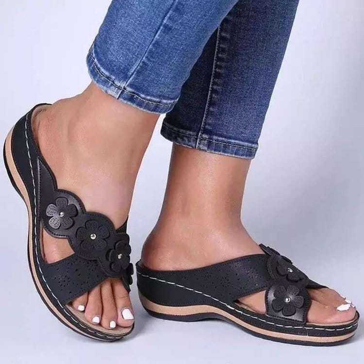 Des sandales compensées en cuir à motif floral rétro avec des embellissements floraux noirs, des lanières en cuir perforées et une semelle beige.