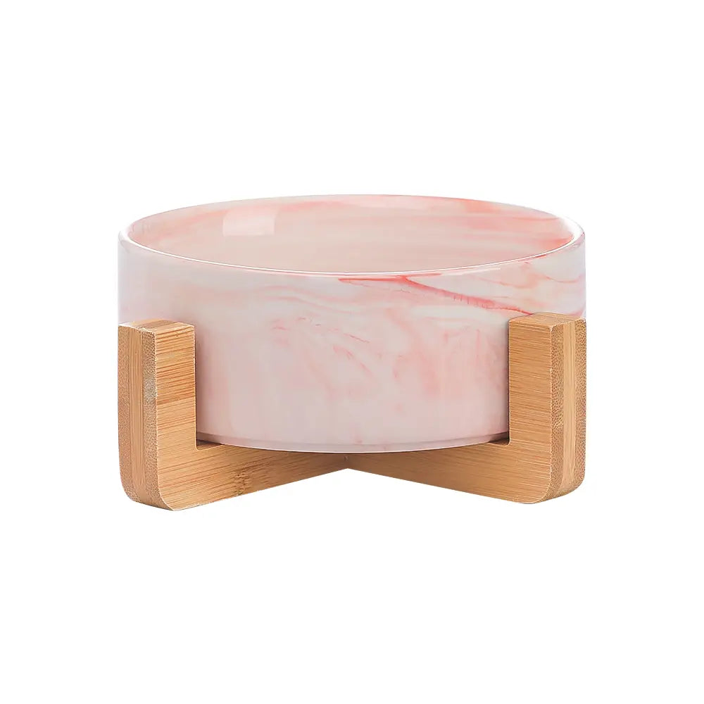 A pink marble-patterned ceramic double pet bowl with a light wood bamboo stand designed for feeding pets.