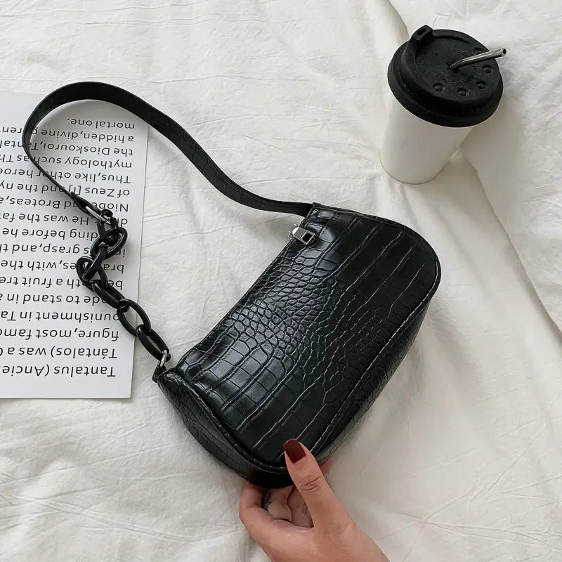 Black crocodile-textured faux leather crossbody bag with a chunky chain strap designed as a croc embossed chain shoulder bag for women.