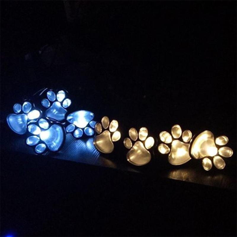 Eine Reihe beleuchteter Solar-Pfotenabdruck-Leuchten mit leuchtenden blauen und warmweißen LED-Akzenten in transluzenten Kunststoffgehäusen für die Außendekoration von Gartenwegen.