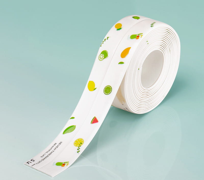 Un rouleau de ruban adhésif d’étanchéité pour cuisine en PVC blanc, anti-moisissure, présentant un motif joyeux de fruits d’agrumes verts et jaunes, des tranches de pastèque et des feuilles, conçu comme une bande d’étanchéité imperméable.