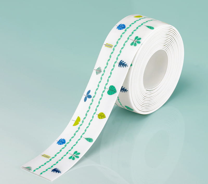Un rouleau de ruban adhésif d’étanchéité pour cuisine en PVC blanc, imperméable et anti-moisissure, présentant un motif ludique de feuilles bleu, vert et jaune avec des lignes pointillées, conçu comme une bande d’étanchéité imperméable.