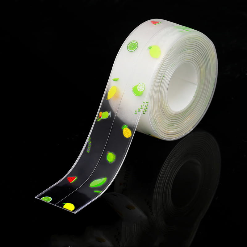 Un rouleau de ruban adhésif d’étanchéité pour cuisine en PVC transparent, anti-moisissure, avec des autocollants de fruits colorés en vert, jaune et rouge sur un support noir, pour une utilisation en bande d’étanchéité imperméable.