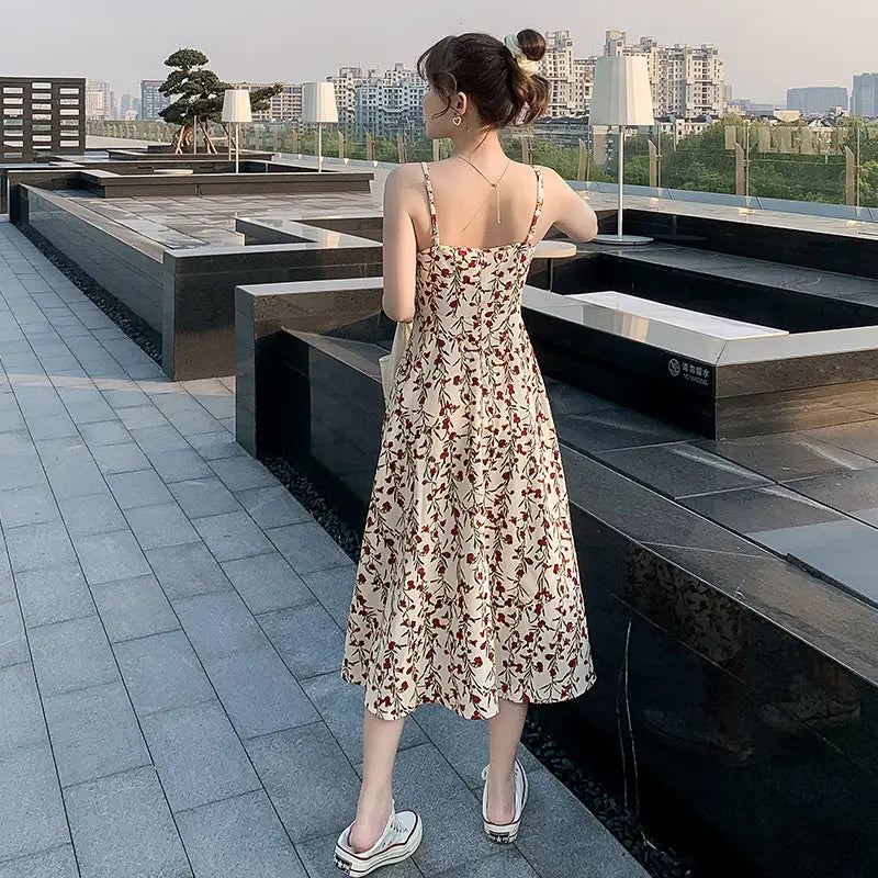 A flowing beige floral print halter midi dress for women featuring delicate red and brown patterns, thin spaghetti straps, and a relaxed fit.