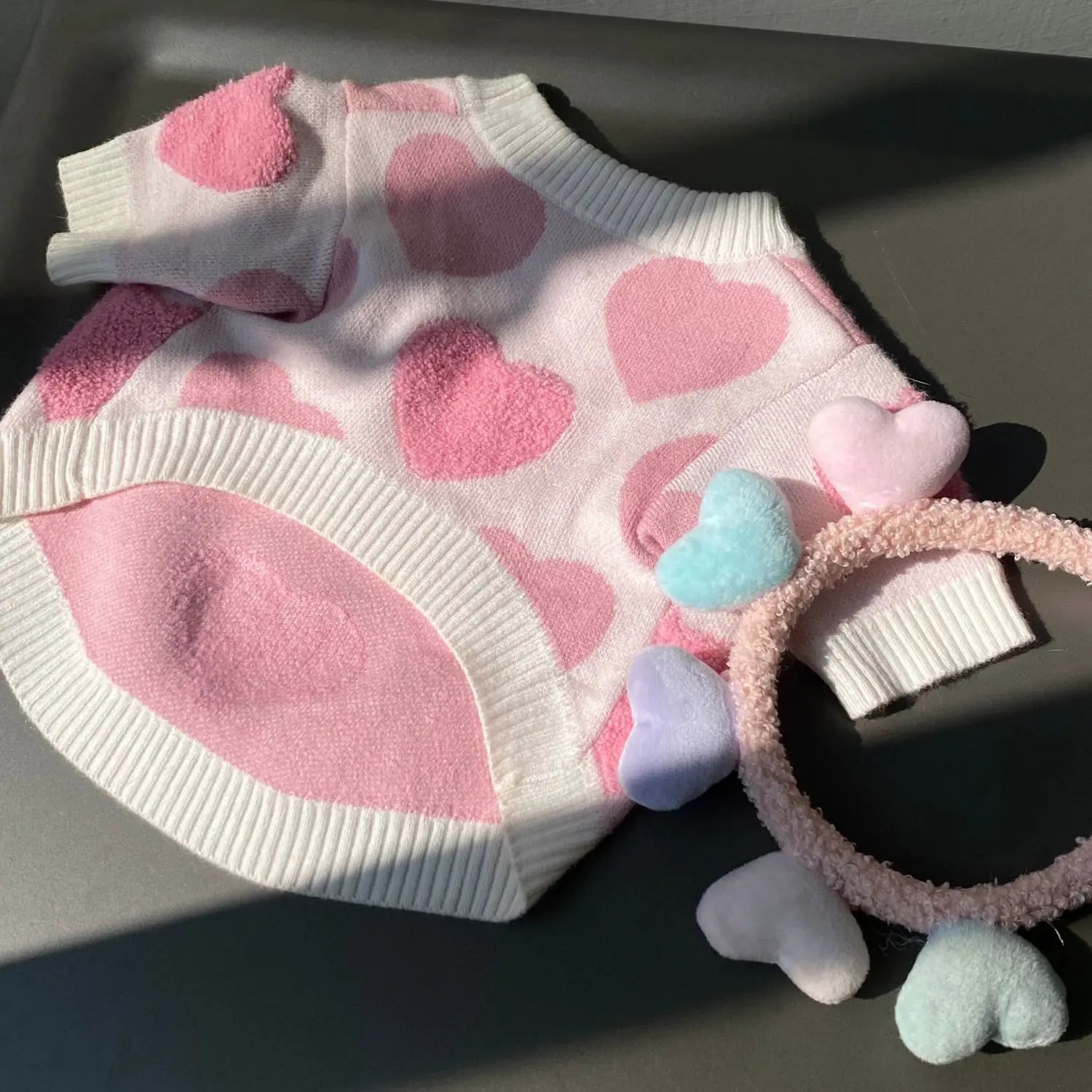 A soft white knit dog heart sweater with pink heart patches and ribbed cuffs designed for winter pet apparel.