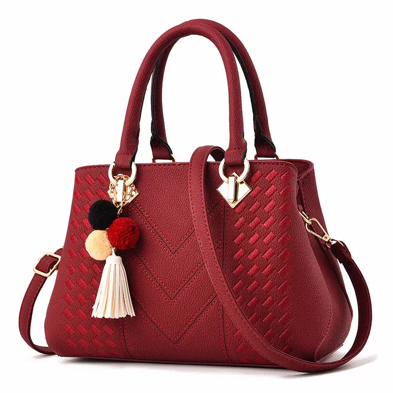A rich burgundy woven PU leather luxury women handbag with a textured chevron pattern, gold-tone hardware, and decorative pom-poms on the handle.