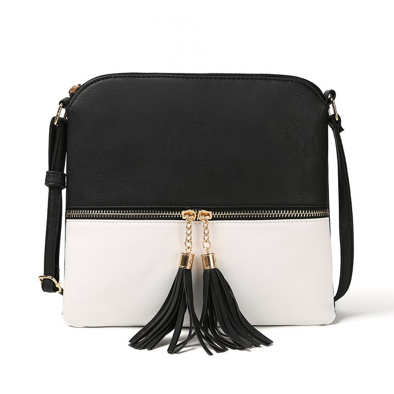 Un sac bandoulière à pompon en simili cuir bicolore noir et blanc avec chaînette de fermeture éclair ton sur ton doré et pompons noirs.
