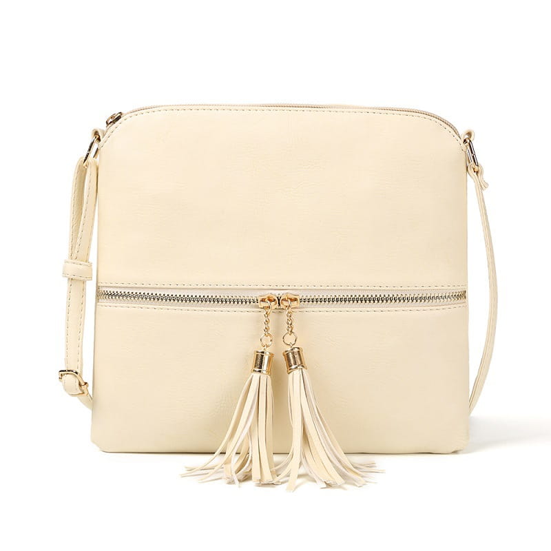 Un sac bandoulière à pompon en simili cuir de couleur crème avec finition lisse, quincaillerie à finition ton sur ton doré et pompons décoratifs sur la chaînette de la fermeture éclair.