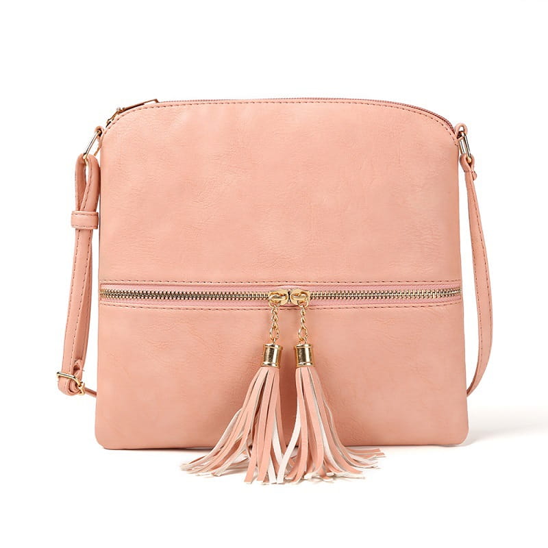 Un sac bandoulière à pompon en simili cuir rose tendre avec une finition type daim, présentant une quincaillerie de fermeture éclair à tons dorés et des pompons décoratifs suspendus à la fermeture éclair avant.