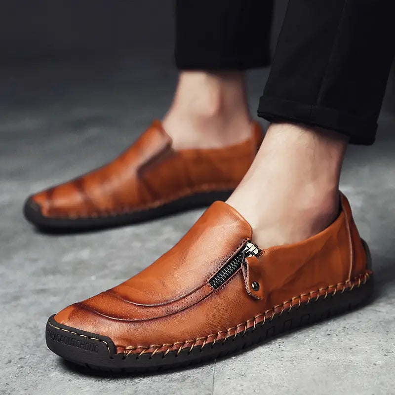 Des mocassins en cuir marron pour hommes, enfiler sans lacets, avec fermeture éclair, et des surpiqûres visibles le long de la semelle, conçus pour un port affaires-décontracté.