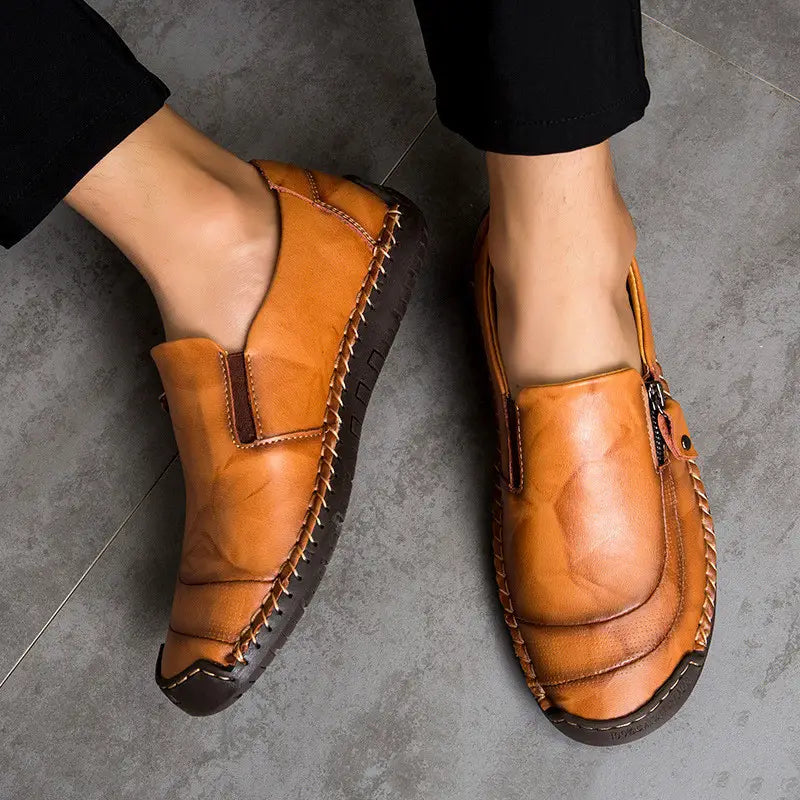 Des chaussures de style affaires-décontracté en cuir pour hommes, type mocassin, avec fermeture éclair, en cuir couleur tan, avec des surpiqûres visibles et une semelle en caoutchouc brun foncé.
