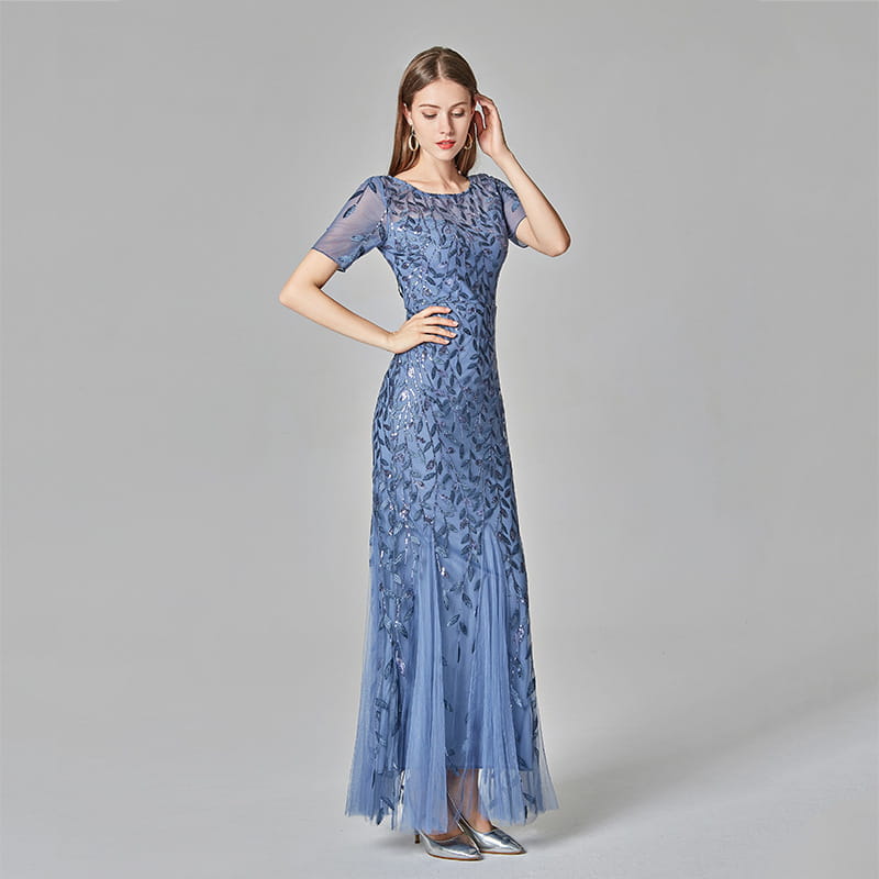 A woman wears a long elegant blue lace embroidered sequin mermaid evening gown with short sleeves and a flowing tulle skirt.